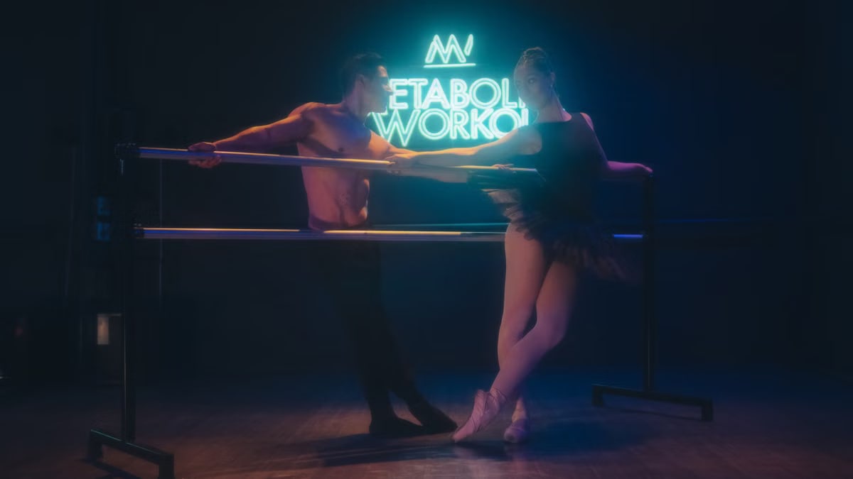 A male and female ballet dancer practicing at the studio bar under neon lights.